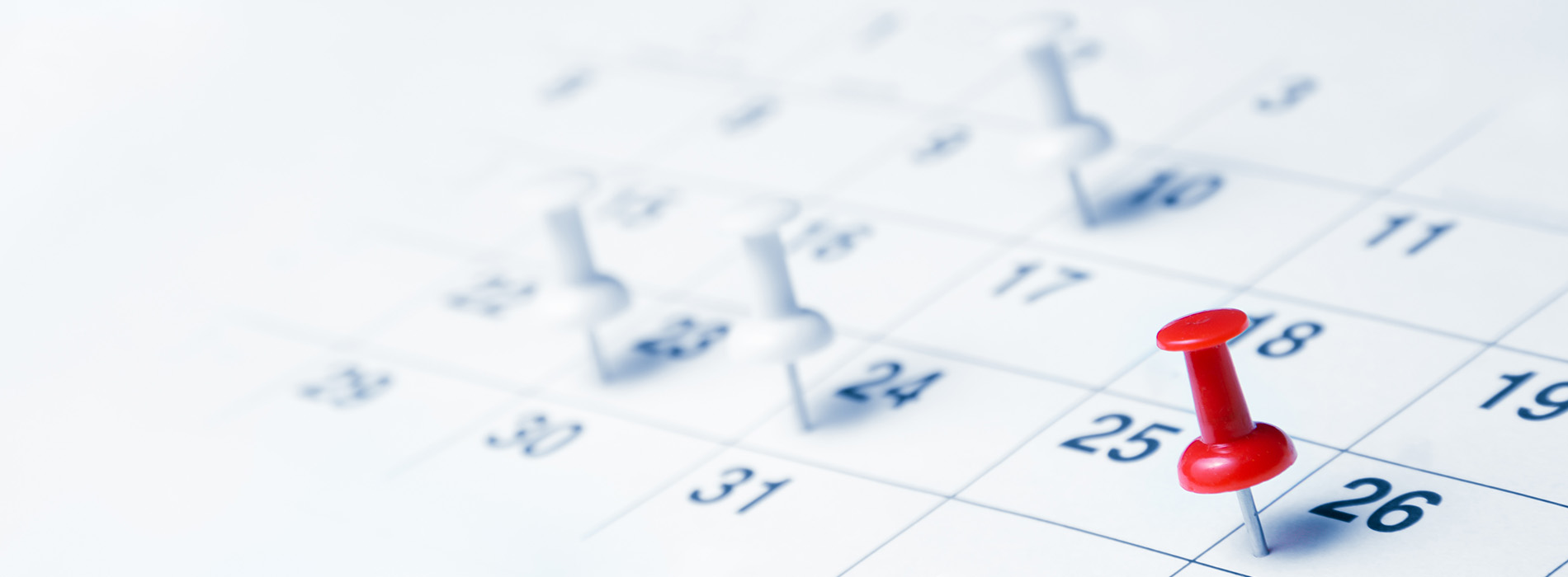 The image shows a close-up of a paper calendar with a red push pin on top, indicating an event scheduled for a specific date.