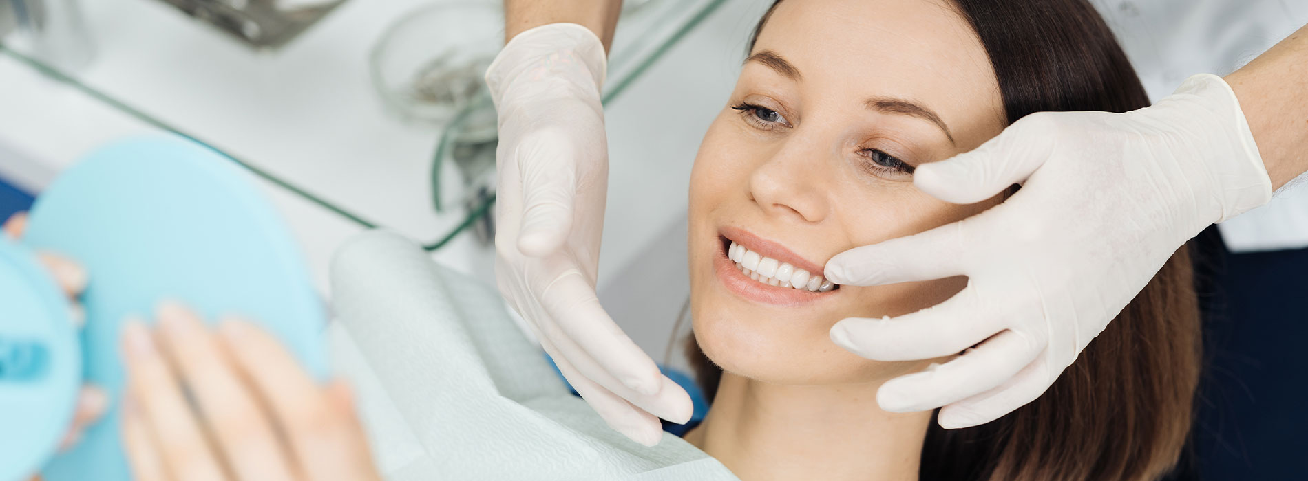 The image shows a woman receiving a facial treatment with a professional s hands applying product while she sits under a magnifying lamp, wearing white gloves.