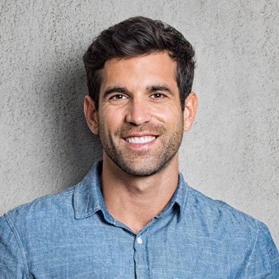 The image features a man smiling at the camera with his arms crossed, wearing a denim shirt and standing against a gray background.