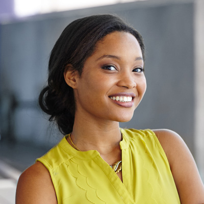 A woman with a radiant smile poses against a backdrop of a concrete wall.