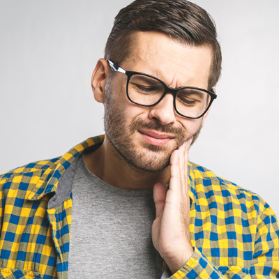 A man with glasses wearing a yellow plaid shirt and holding his hand to his mouth, possibly in disbelief or concern.