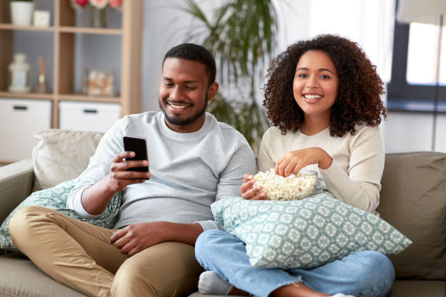A man and woman sitting on a couch, sharing a moment together while watching something on a phone.